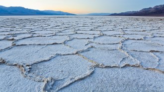 A photo of the salt flats in Badwater Basin in Death Valley, California in the foreground with mountains and sky in the background.