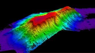 An elevation image of Kelvin Seamount, in a rainbow of color with purple at the bottom and red at the top, on a black background.