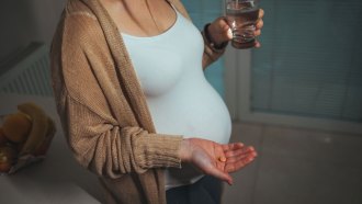 pregnant person holding a pill in one hand and a glass of water in the other hand