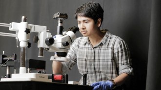 A photo of Deblina Sarkar standing behind a table with a big microscope on it.