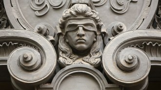 A close up photo of detail on a building showing the sculpture of a head with a blindfold covering the person's eyes.