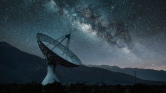 A photo of a radio telescope pointing toward the night sky where the milky way can be seen.