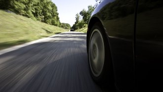 A close up photo of a car's tire while it drives on a black top road.