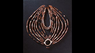 An ornate neckleace made of multiple symmetrical strings of beads, with a pendant and mother-of-pearl-ring at opposite ends