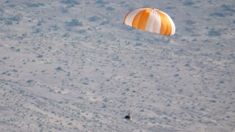 A photo of a small space capsule parachuting down to land in Utah.