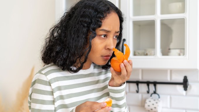 A woman sniffs a half-peeled tangerine in her kitchen.
